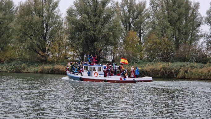 Een boot met passagiers vaart langs de oever van een rivier in een groene omgeving.