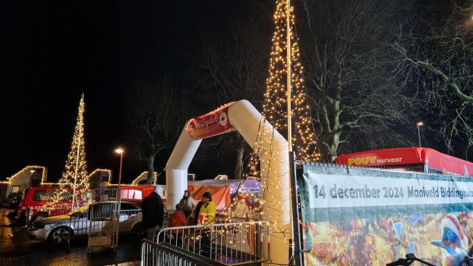 Sfeervolle kerstmarkt met verlichte bomen en een feestelijke toegangspoort.