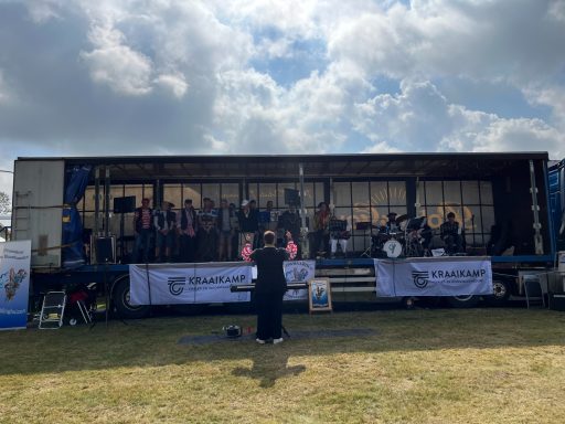 Een band speelt op een vrachtwagen, met een toeschouwer vooraan in een open veld.