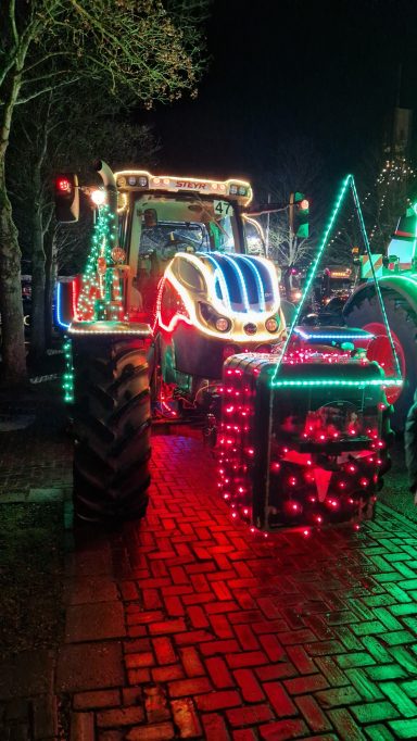 Kleurige versierde tractor met lichtjes, op een straat verlicht door de nacht.