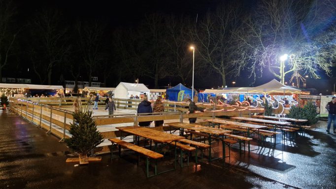 Nachtelijke markt met houten tafels en kramen onder verlichting.