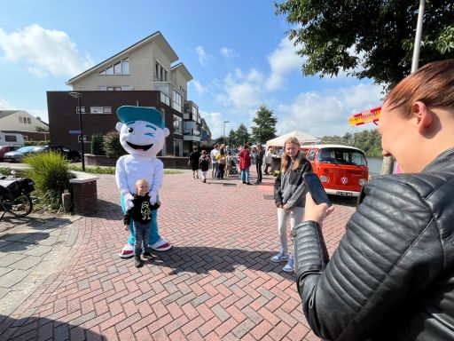 Een persoon in een mascottenkostuum poseert met een kind op een drukke straat.