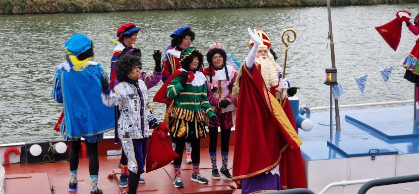 Kinderen in kleurrijke kostuums ontmoeten Sinterklaas aan boord van een boot.
