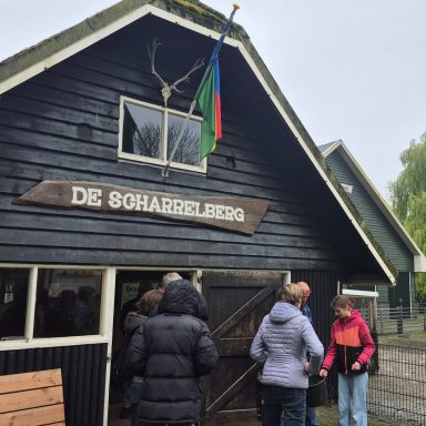 Groepsactiviteit bij een houten gebouw met een vlag en een bord met de naam "De Soharelling".