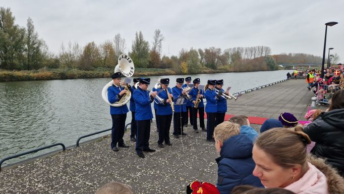 Een blaaskapel speelt aan de waterkant, kijkers staan in de voorgrond.