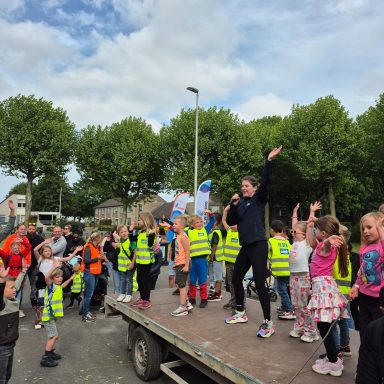 Kinderen en volwassenen vieren samen op een vrachtwagen, vrolijke atmosfeer met vlaggen.