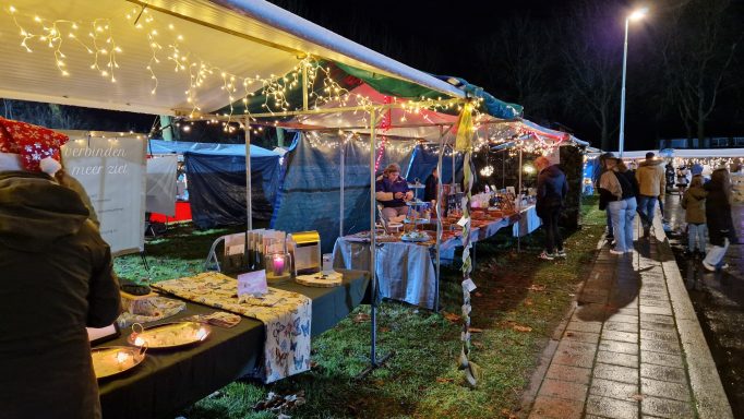 Kraampjes op een avondmarkt, verlicht door lampjes en met bezoekers die rondlopen.