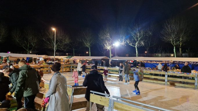 Drukke ijsbaan met mensen die schaatsen in de avond onder lichtjes en bomen.