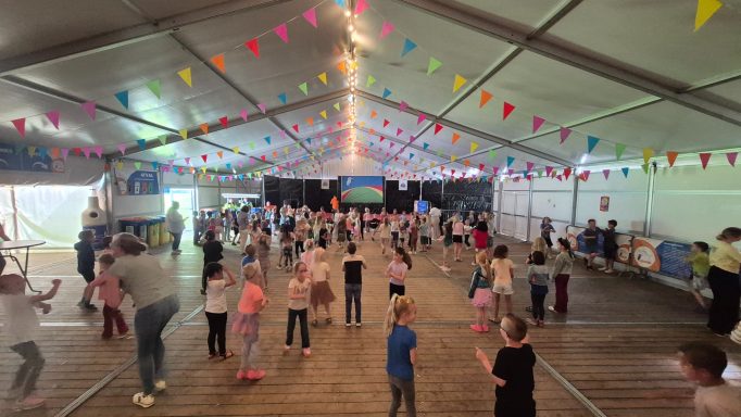 Kinderen dansen en spelen in een versierde tent met gekleurde vlaggen.