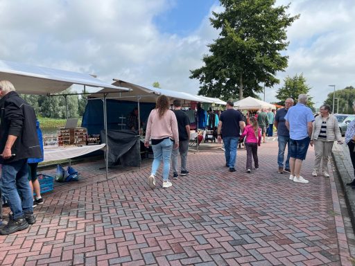 Drukke marktdag met bezoekers en kraampjes langs een geplaveide weg.