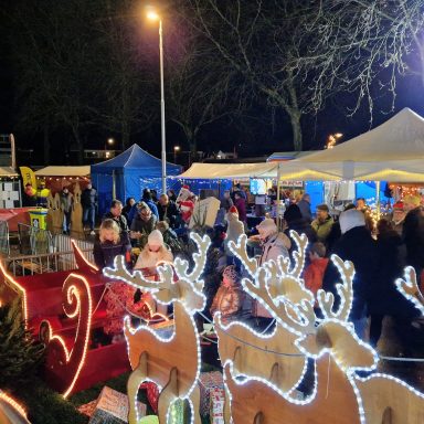 Drukke kerstmarkt met feestelijke verlichting en kramen in een stadsomgeving.