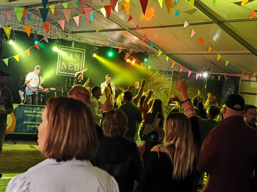 Een muzikale gebeurtenis met een band en publiek in een tent, versierd met vlaggetjes.