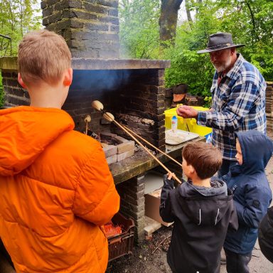 Volwassen man met hoed helpt kinderen bij het roosteren van voedsel boven een open vuur.